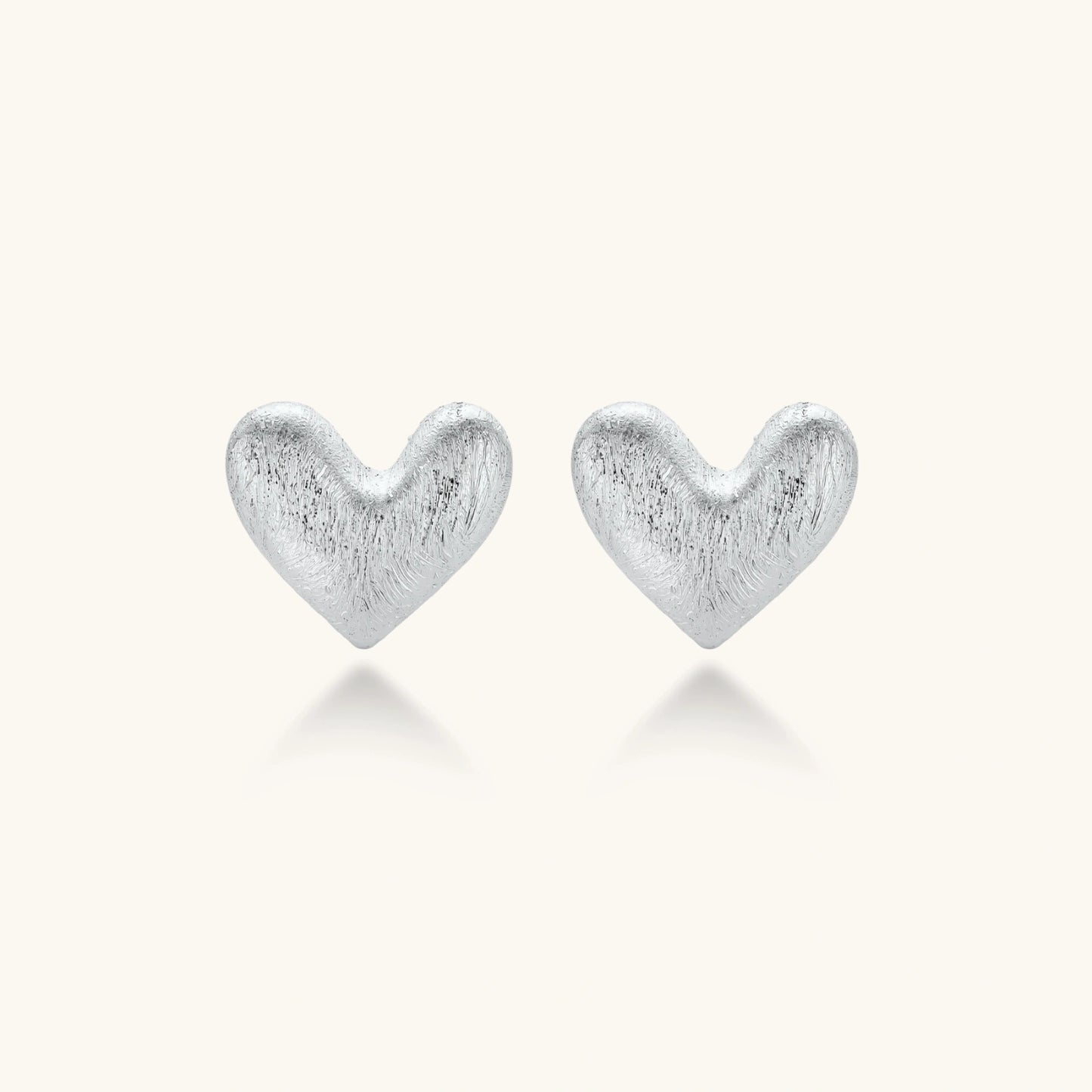 Pair of brushed platinum-plated 925 sterling silver puffy heart stud earrings on a cream background.