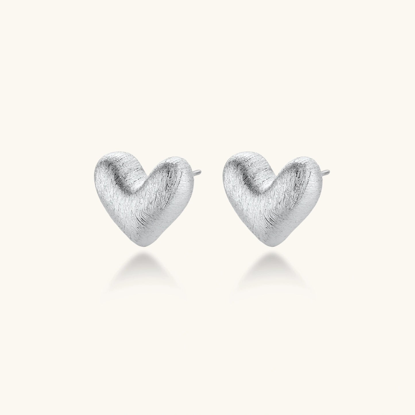 Pair of brushed platinum-plated 925 sterling silver puffy heart stud earrings on a cream background.