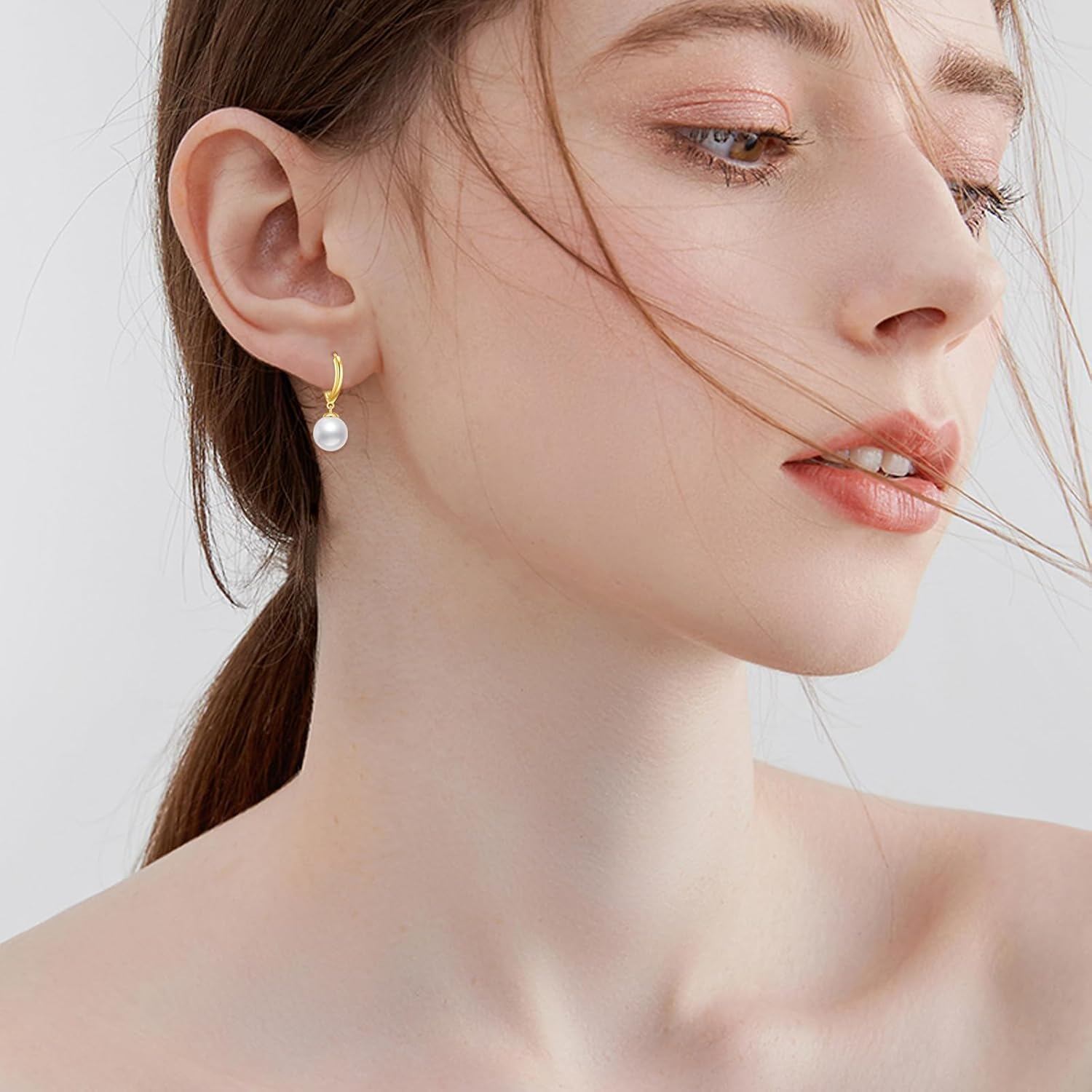 Model wearing solid 14K gold drop hoop earrings with freshwater cultured pearls.